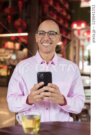 Bald Hispanic man wearing pink casual business shirt and eyeglasses in Chinese style tea house 129841352