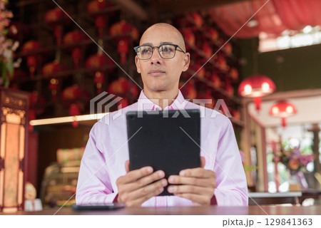 Bald Hispanic man wearing pink casual business shirt and eyeglasses in Chinese style tea house Bald Hispanic man wearing pink casual business shirt and eyeglasses in Chinese style tea house 129841363