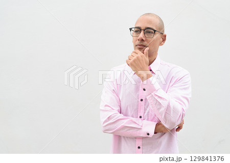 Bald Hispanic man wearing pink casual business shirt and eyeglasses thinking and looking up 129841376
