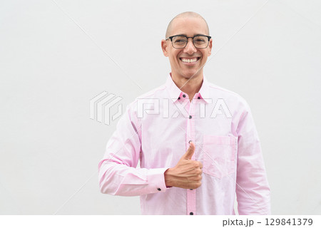 Bald Hispanic man wearing pink casual business shirt and eyeglasses with thumb up gesture 129841379