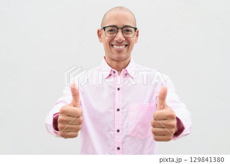 Bald Hispanic man wearing pink casual business shirt and eyeglasses with thumb up gesture Bald Hispanic man wearing pink casual business shirt and eyeglasses with thumb up gesture 129841380