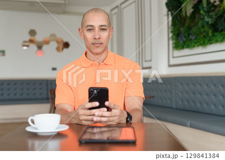 Bald Hispanic businessman having coffee break in cafe and using phone 129841384