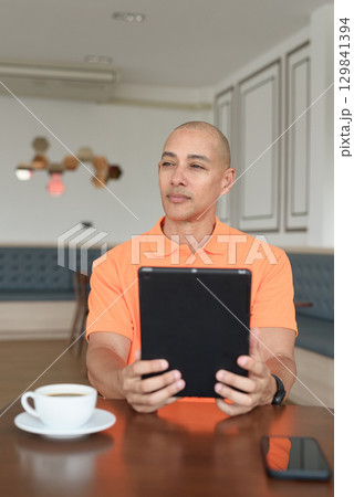 Bald Hispanic man using digital tablet computer and thinking in coffee shop Bald Hispanic man using digital tablet computer and thinking in coffee shop 129841394