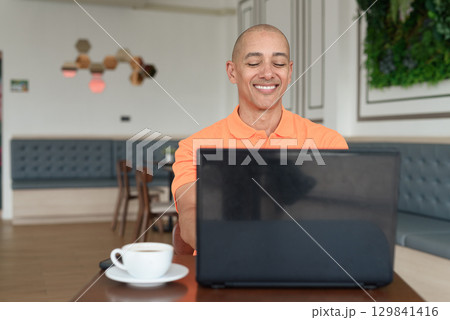 Happy bald Hispanic man smiling and using laptop computer in coffee shop restaurant Happy bald Hispanic man smiling and using laptop computer in coffee shop restaurant 129841416