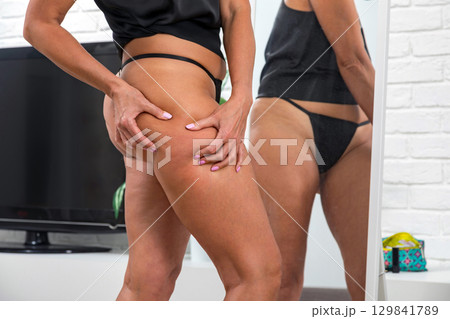 Woman in black underwear touching her thigh in front of mirror at home 129841789