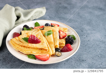 Golden crepes with fresh berries on a blue background. Breakfast. Dessert. Golden crepes with fresh berries on a blue background. Breakfast. Dessert. 129841795