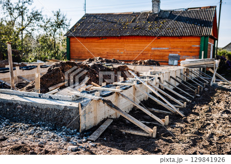 Building strip foundation for new house near old wooden house 129841926