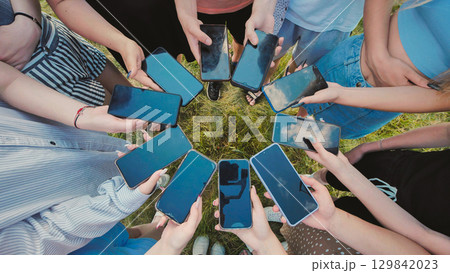 Students gathering on the grass after school, sharing content and enjoying time together with their smartphones 129842023