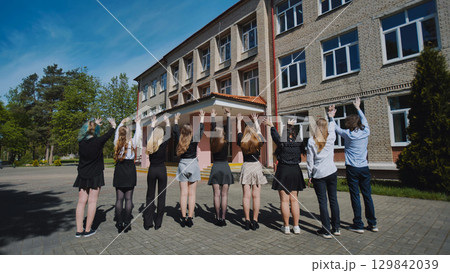 Group of happy students waving goodbye to their school on the last day, celebrating the end of the academic year Group of happy students waving goodbye to their school on the last day, celebrating the end of the academic year 129842039