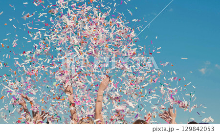 High school students joyfully celebrating graduation by tossing colorful confetti under a clear blue sky 129842053