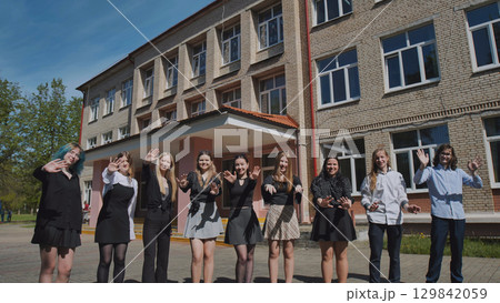Students happily waving in front of school building on sunny day, marking the end of the school year with joy Students happily waving in front of school building on sunny day, marking the end of the school year with joy 129842059