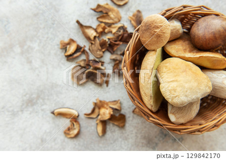 Fresh mushrooms overflowing from wicker basket onto table with dried mushrooms Fresh mushrooms overflowing from wicker basket onto table with dried mushrooms 129842170