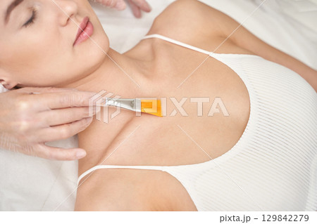 Female getting skincare cosmetic treatment with brush on chest in spa setting Female getting skincare cosmetic treatment with brush on chest in spa setting 129842279