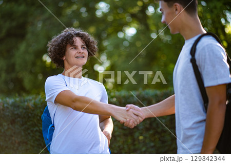 Two friends meeting, shaking hands and looking pleased Two friends meeting, shaking hands and looking pleased 129842344
