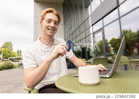Redhead businessman making purchase using laptop filling out checkout Redhead businessman making purchase using laptop filling out checkout 129842368