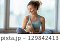 Smiling woman in sportswear cuddling a cute orange kitten indoors 129842413