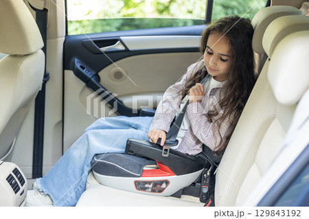 Dark-haired girl of school age sitting in a care with her seatbelt fixed 129843192