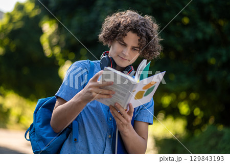 Curly-haired teen with a book in hands in the park 129843193