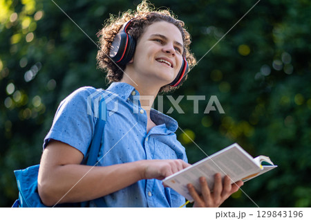 Curly-haired teen with a book in hands in the park 129843196