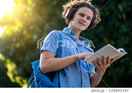 Curly-haired teen with a book in hands in the park 129843197