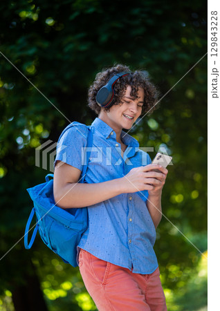 Curly-haired teen in blue shirt in the park looking contented 129843228