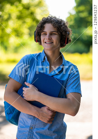 Teen in blue thsirt in the park with headphones and books in hands Teen in blue thsirt in the park with headphones and books in hands 129843237
