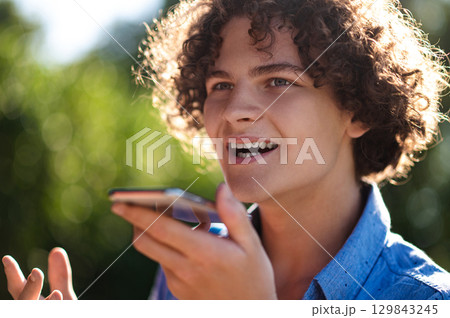 Curly-haired teen with a phone in hands in the park 129843245