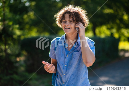 Curly-haired teen with a phone in hands in the park 129843246