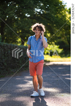 Curly-haired teen with a phone in hands in the park 129843247