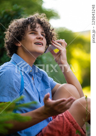 Curly-haired teen in blue tshirt spending time in the park 129843248