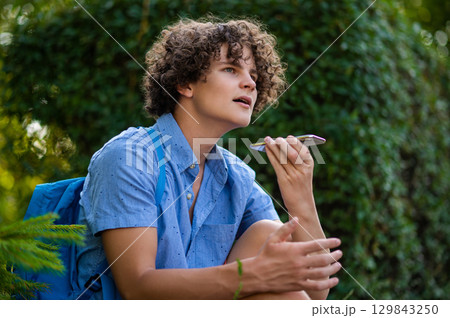 Curly-haired teen in blue tshirt spending time in the park 129843250