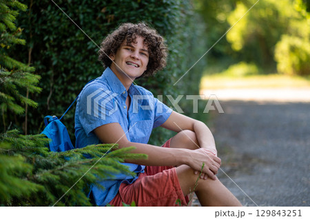 Curly-haired teen in blue tshirt spending time in the park 129843251