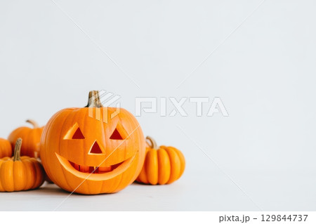 A cheerful Halloween Pumpkin surrounded by little Mini Pumpkins on a clean White Background 129844737