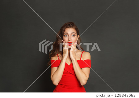 Surprised woman with curly hairstyle and makeup holding her hand with her face on black background Surprised woman with curly hairstyle and makeup holding her hand with her face on black background 129845065