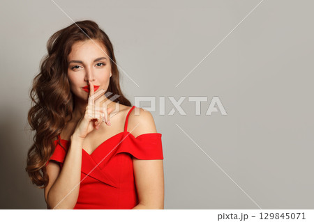 Pretty charming young woman having secret while holding finger on lips and showing silence sign 129845071