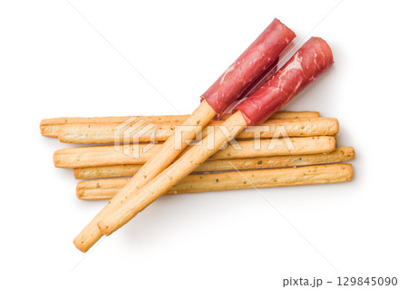Slices of smoked bresaola and grissini sticks isolated on white background. 129845090