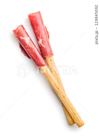 Slices of smoked bresaola and grissini sticks isolated on white background. 129845092