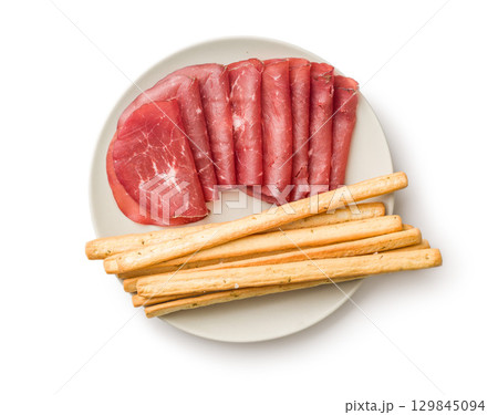 Slices of smoked bresaola and grissini sticks isolated on white background. Slices of smoked bresaola and grissini sticks isolated on white background. 129845094