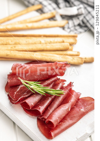 Slices of smoked bresaola on white table. 129845211