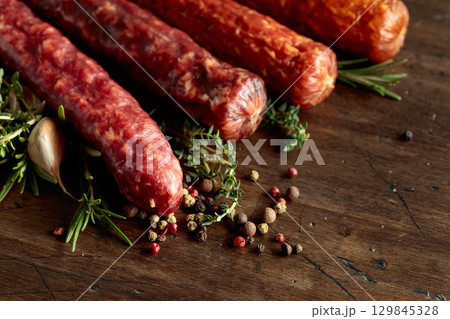 Various dry cured sausages with spices on a old wooden table. 129845328