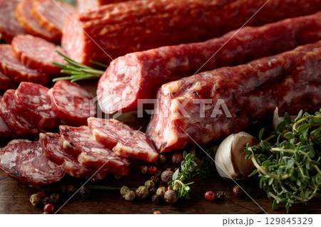 Sliced dry cured sausages with spices on a old wooden table. Sliced dry cured sausages with spices on a old wooden table. 129845329