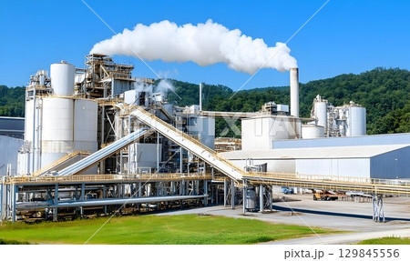 Industrial complex billowing smoke against a backdrop of green forest hills 129845556