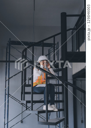 Construction manager and engineer dressed in orange work vests and hard helmets explore construction documentation on the building site near the steel frames 129846003