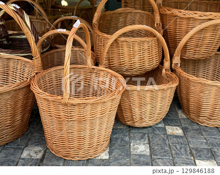 Numerous empty wicker baskets of various sizes and shapes, each featuring sturdy handles, are arranged on a cobblestone street, highlighting traditional craftsmanship 129846188