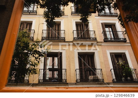 An old European building facade with windows and balconies in warm colors, bathed in sunlight. View of an old building facade featuring windows with black shutters and balconies. European city street. 129846639