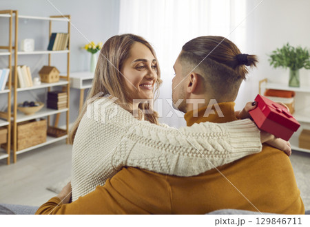 Happy woman holding red present box in her hand and hugging her boyfriend. Happy woman holding red present box in her hand and hugging her boyfriend. 129846711