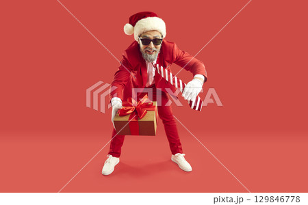 Man in red suit and Santa hat standing on red background and giving you Christmas present Man in red suit and Santa hat standing on red background and giving you Christmas present 129846778