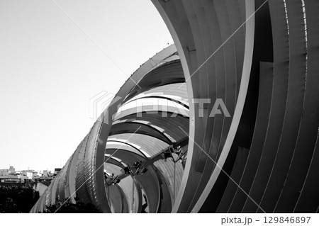 A monochrome image capturing architectural curves and lines in a modern structure. Black and white architectural detail of a modern building, showing curved lines and abstract shapes under sunlight. A monochrome image capturing architectural curves and lines in a modern structure. Black and white architectural detail of a modern building, showing curved lines and abstract shapes under sunlight. 129846897