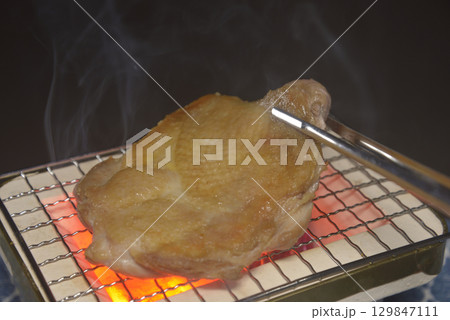煙りの立ち昇る七輪で鶏モモ肉を焼く 129847111