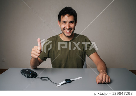Cheerful male demonstrating positive sign while powering smartwatch through portable charger, signaling technological convenience and personal satisfaction. Concept of healthy lifestyle. Cheerful male demonstrating positive sign while powering smartwatch through portable charger, signaling technological convenience and personal satisfaction. Concept of healthy lifestyle. 129847298
